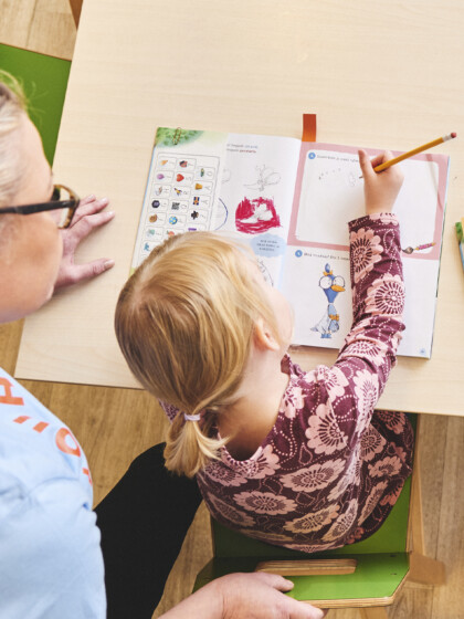 Päiväkodin työntekijä auttaa lasta tekemään tehtäväkirjaa